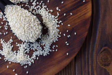 Tahta arka planda siyah kaşıkta beyaz susam tohumları.