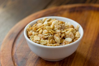 Tahta masanın üzerinde beyaz seramik kâse içinde granola veya müsli.