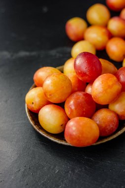 Güzel olgun yaban erikleri seramik tabakta siyah arka planda