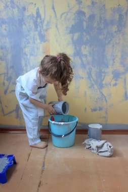 Küçük çocuk boya fırçasıyla eğleniyor, duvarları boyayla yenilemeye yardım ediyor.