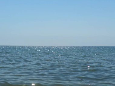 Sonu gelmeyen mavi okyanus ile sakin deniz manzarası ufukta berrak gökyüzü, sakin ve huzurlu atmosferli minimalist kıyı manzarası.