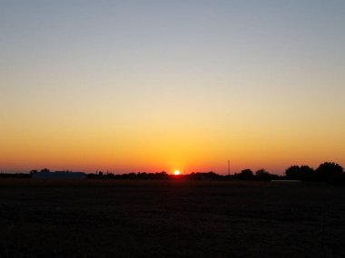 Gün batımında kırsal alan, ekinlerin üzerinde gün ışığının azalmasıyla parlayan turuncu ufuk..