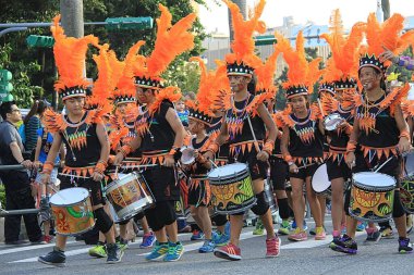 Taipei, Taiwan - October 17, 2015: Children in vibrant tribal-inspired costumes with orange feathered headdresses play drums in a lively street parade. The group marches joyfully past onlookers during a colorful cultural celebration