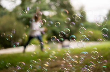 Mutlu kız yaz parkında sabun köpüğüyle oynuyor.