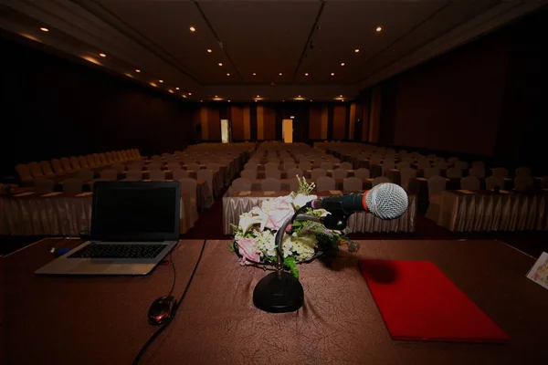 The microphone is located on podium stand at the center of the room is covered with a red carpet with a white tables cloth and chairs and prepare before the start of  seminar meeting.