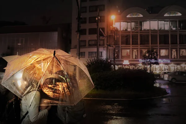 Die Paare werden sich nachts unter dem durchsichtigen Regenschirm küssen. — Stockfoto