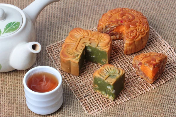 Round mooncake 8 grains and salted eggs and squred mooncake filled red beans, stirred in green tea and chopped macadamia nuts served with tea and teapot.