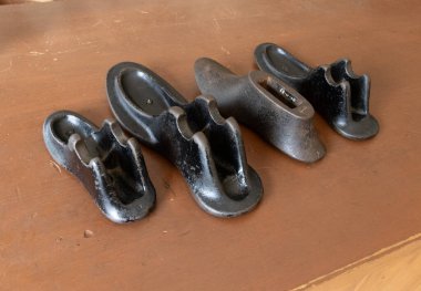 Eski dökme demir ayakkabı seti ahşap bir yüzey üzerinde sergilenir. Bu aletler geleneksel olarak ayakkabı yapımı ve onarımında kullanılır, deri ayakkabıları şekillendirmek ve onarmak için sağlam bir form sağlar..