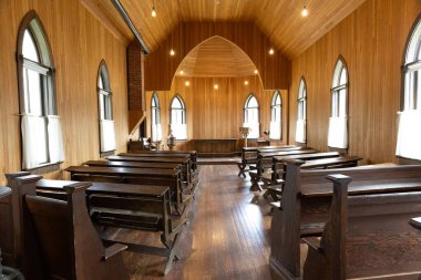 Parlak ahşap zeminleri, yüksek kavisli tavanı ve mihraba bakan siyah ahşap sıraları olan tarihi ahşap bir kilisenin içi. Sıcak doğal ışığı olan sakin ve basit bir dini mekan..