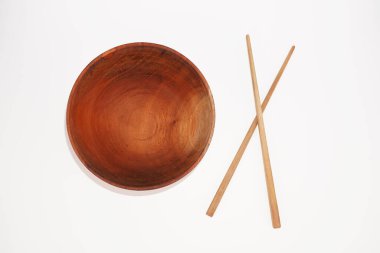 Koyu renk ahşap bir kase beyaz arka planda iki çapraz çubuğun yanında oturur..