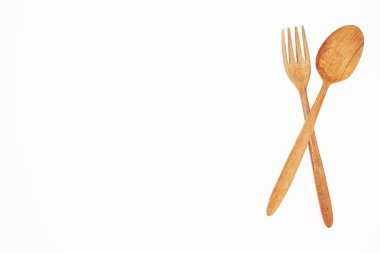 Açık kahverengi bir ahşap kaşık ve çatal beyaz arka planda kesişir..