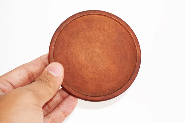 Bir el yuvarlak, koyu kahverengi, ahşap bir tabak tutar..