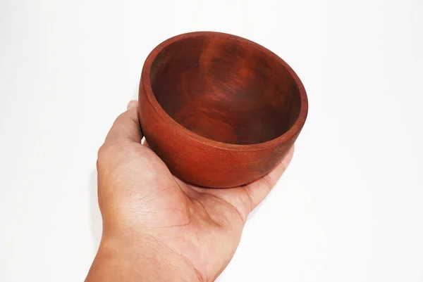 Bir insan, koyu kahverengi ahşaptan yapılmış boş bir kase tutar..