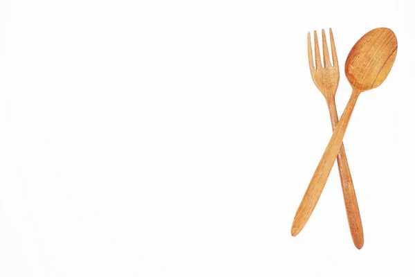 Açık kahverengi bir ahşap kaşık ve çatal beyaz arka planda kesişir..