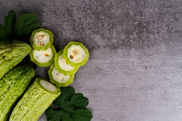 Gri arkaplanda yaprakları olan dilimlenmiş ve acı kavunlar.