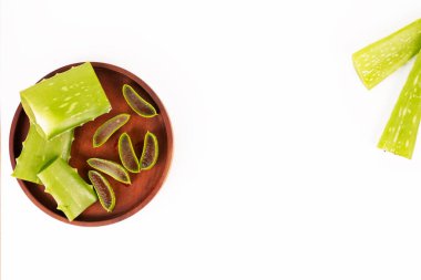 Kahverengi ahşap bir tabakta taze bir aloe vera bitkisinin kesilmiş parçaları bulunur..