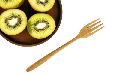 Tahta bir çatal, dört taze, dilimlenmiş kivi yarısıyla kahverengi bir ahşap tabağın yanında oturur..