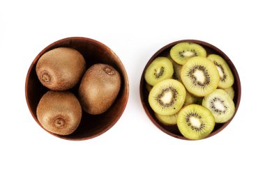 Two brown wooden bowls hold whole kiwis and freshly cut kiwi slices on a white background.