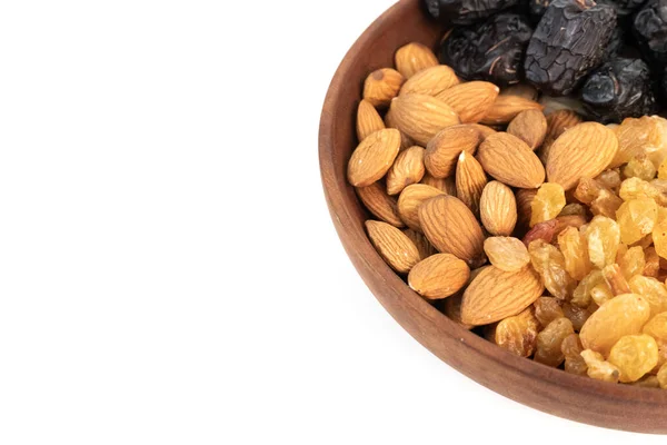 Tahta bir kase beyaz arka planda hurma, badem, fıstık ve kuru üzüm barındırır..