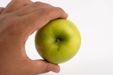 Bir insanın eli beyaz arka planda taze, yuvarlak yeşil bir elmayı tutar..