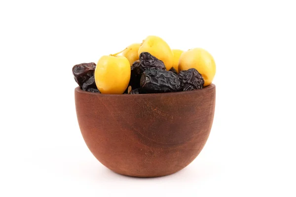 Küçük kahverengi bir ahşap kase koyu ve sarı hurmalarla doludur..