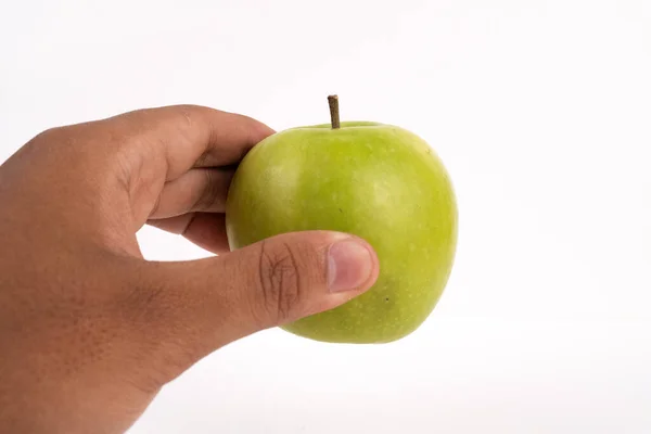 Bir insanın eli, beyaz bir arka planda taze koparılmış yeşil bir elmayı tutuyor..
