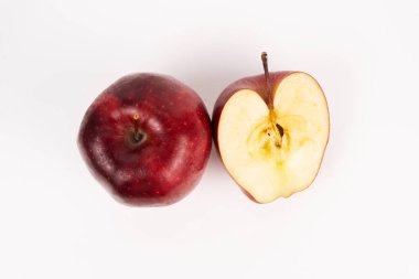 Tüm kırmızı elma, yukarıdan beyaz bir yüzey üzerinde, dilimlenmiş yarım yamalak yıldız deseninin yanında duruyor..