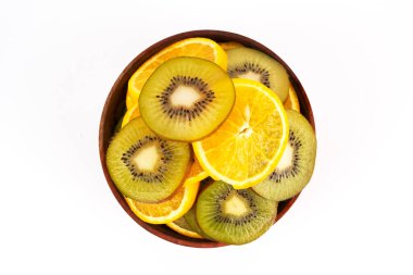 Dilimlenmiş kivi ve portakal, beyaz arka plan karşısında parlak renklere sahip yuvarlak bir ahşap kaseyi doldurur..