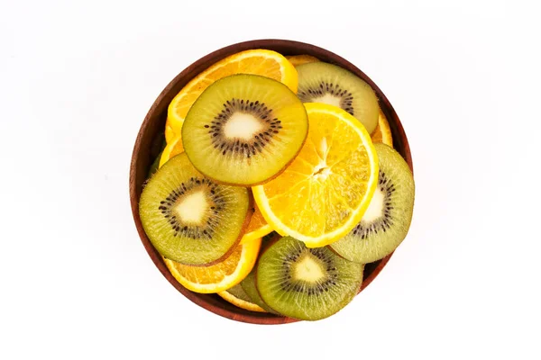 Dilimlenmiş kivi ve portakal, beyaz arka plan karşısında parlak renklere sahip yuvarlak bir ahşap kaseyi doldurur..