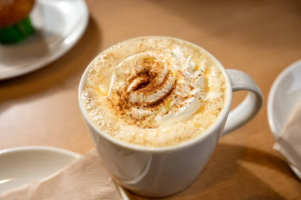 Ahşap bir kafe masasında beyaz bardakta servis edilen kremalı, taze yapılmış balkabağı aromalı latte kahve. Yüksek kalite fotoğraf
