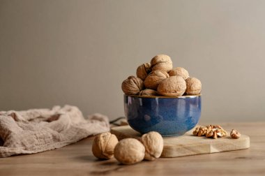 Yumuşak kumaşlı ahşap bir kesme tahtasının üzerinde mavi bir seramik kasede duran cevizlerin kırsal yaşam bileşimi. Sıcak sıcak yemek arka planı.