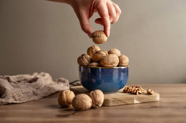 Tahta kesme tahtasındaki mavi seramik ceviz kasesine uzanan bir elin yakın çekimi. Doğal sonbahar durgun yaşam arka planı.