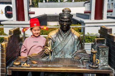 Genç bir kız bambu kitabının üzerine Acient Çin bursu heykelinin yanında oturuyor.. 