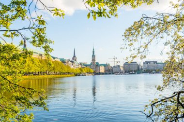 Almanya, Hamburg 'da gün batımının altında bulutlu gökyüzü olan Alster Gölü kıyısında güzel bir bina..