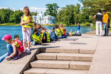 School kids at the lakeshore of the Great Pond in the Catherine Palace , a Rococo palace, the summer residence of the Russian tsars in St. Petersburg, Russia clipart