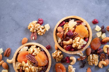 Sağlıklı atıştırmalıklar: ahşap kasede karışık fındık ve kurutulmuş meyve koyu çimento masa zemininde, badem, ananas, kızılcık, papaya, elma, çilek, vişne, kayısı, kaju.