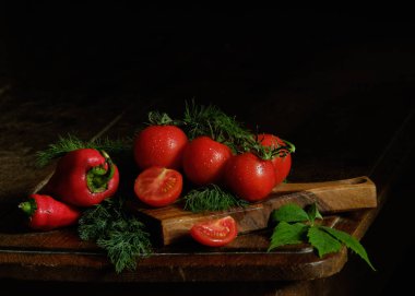 Durgun hayat. Kırmızı domatesler ve yeşillik siyah arka planda bir masada. Düşük tuşlu fotoğraf