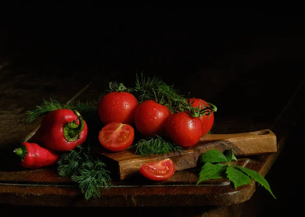 Натюрморт. Червоні помідори та зелень на столі на чорному тлі. Фотографія з низьким ключем — стокове фото
