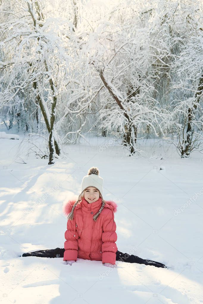 Caucasian little girl in a pink coat sits twine on the snow in the park. sunny winter day in the park. snowy winter