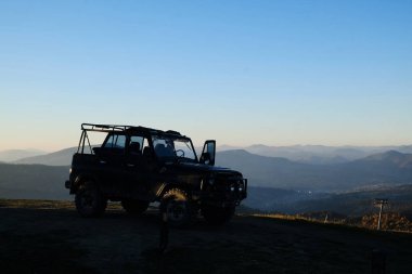 Gün batımında bir SUV arabası bir dağın tepesinde duruyor..