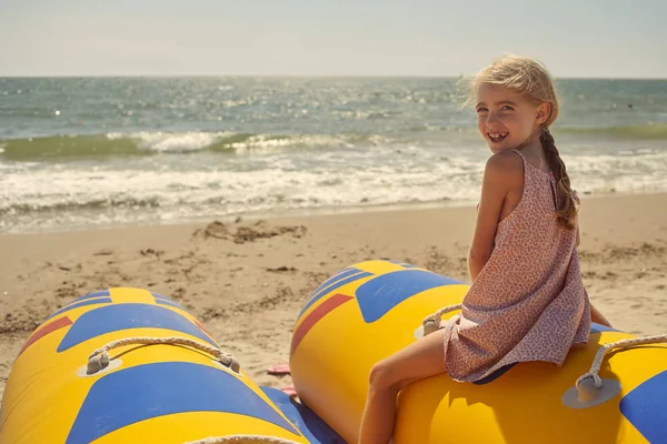 Sarışın, neşeli kız deniz kenarında bir teknede oturuyor..