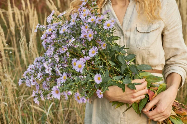 Bouquet of lilac small flowers in the hands of a woman on a blurred natural background