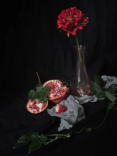 Red flower in a vase and pomegranates on a black background