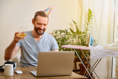 Parti online. Şapkalı beyaz bir adam doğum gününü arkadaşlarıyla kutlar. Adam zevkle monitöre bakar ve bardağını kaldırır..