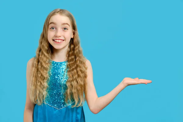 Fröhliche kleine schöne kaukasische Mädchen in einem blauen Kleid hält ihre Hand zur Seite, Handfläche nach oben. Das Konzept von Werbeartikeln und Kopierfläche. — Stockfoto