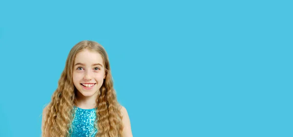Ein wunderschönes fröhliches kleines kaukasisches Mädchen in einem wunderschönen blauen Kleid blickt in die Kamera. Vereinzeltes halblanges Porträt auf blauem Hintergrund und Kopierraum. — Stockfoto