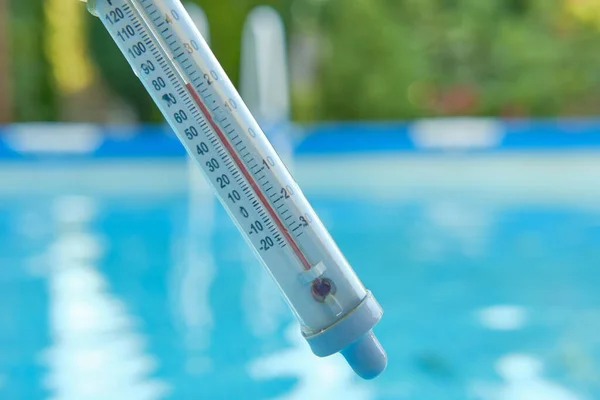 Termómetro que mide la temperatura del agua para nadar sobre un fondo borroso de agua azul en la piscina. Concepto de verano. — Foto de Stock