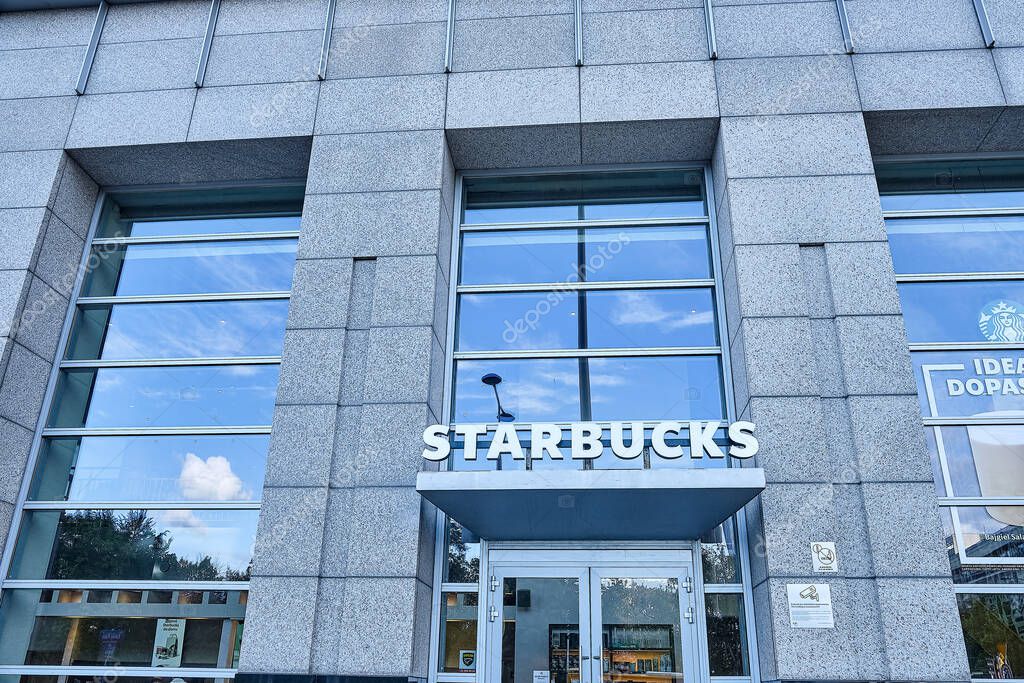 Warsaw, Poland. August 2025. Entrance to a Starbucks coffee shop in a modern glass and concrete building. The reflection of the clouds can be seen in the windows.