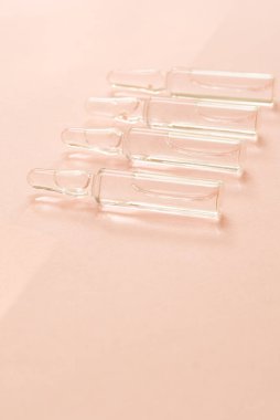 Yumuşak pembe arkaplana yerleştirilmiş sıvı dolu şeffaf cam ampuller güzellik tedavilerini, cilt serumlarını veya ilaç çözümlerini sembolize eder. Boşluğu kopyala