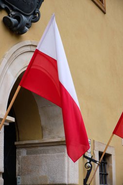 Varşova, Polonya, 14 Eylül 2025. Varşova 'daki klasik Old Town binası cephesinde Polonya bayrağı. Bayrak, hafif taş kemerin yanında asılı, desenli sarı alçı, küçük pencere ve siyah işlemeli demir fikstür.